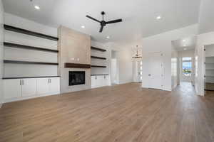 Unfurnished living room featuring ceiling fan, a chandelier, light wood-style floors, a tiled fireplace, and recessed lighting