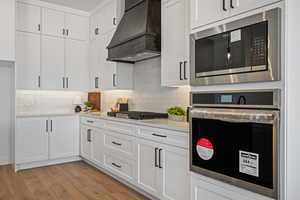 Kitchen with stainless steel appliances, premium range hood, white cabinets, and decorative backsplash