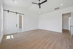 Unfurnished bedroom with a barn door, light wood finished floors, baseboards, vaulted ceiling, and recessed lighting