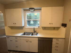 Kitchen with dishwasher, a sink, light countertops, and white cabinetry