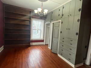 Main floor bedroom with a chandelier and dark wood finished floors and built in drawers.
