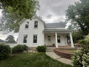 View of front of property with covered porch, a shingled roof, brick siding, and a front yard