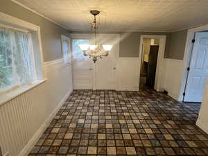 Possible dining area with wainscoting, a chandelier, a textured ceiling, ornamental molding, and baseboards