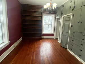 Unfurnished dining area featuring dark wood-style floors, a chandelier, baseboards, plenty of natural light, and crown molding