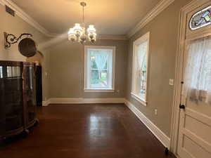 Unfurnished living room featuring arched walkways, a chandelier, dark wood finished floors, crown molding, and baseboards