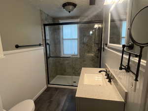 Remodeled Bathroom featuring a stall shower, toilet, wood finished floors, vanity, and a wainscoted wall