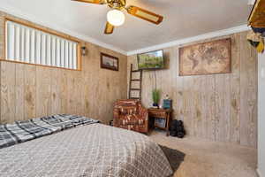 Bedroom with carpet, wood walls, a textured ceiling, crown molding, and ceiling fan