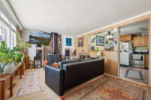 Living room with a wood stove, a textured ceiling, ceiling fan, and light colored carpet