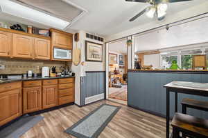 Kitchen with white microwave, light wood-type flooring, a ceiling fan, a wainscoted wall, and brown cabinetry