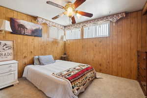 Bedroom with carpet, wood walls, and ceiling fan