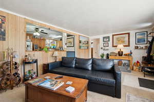 Living area with light carpet, a ceiling fan, wooden walls, and a textured ceiling