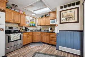 Kitchen featuring white appliances, a sink, wainscoting, dark countertops, and light wood-style floors