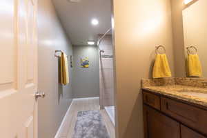 Full bath featuring a tile shower, vanity, tile patterned flooring, and baseboards