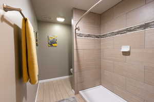 Full bathroom featuring a tile shower, toilet, baseboards, and wood finish floors