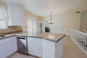 Kitchen with stainless steel dishwasher, a peninsula, healthy amount of natural light, and a chandelier