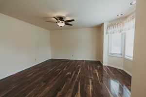 Empty room featuring dark wood-style flooring, ceiling fan, and baseboards