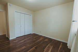Unfurnished bedroom with dark wood-style flooring, baseboards, and a closet