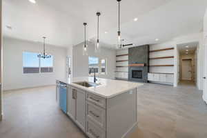 Kitchen with a sink, a chandelier, stainless steel dishwasher, a tiled fireplace, and plenty of natural light