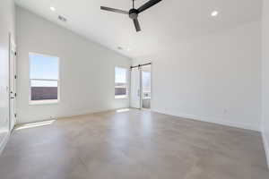 Spare room with finished concrete floors, lofted ceiling, a ceiling fan, baseboards, and a barn door
