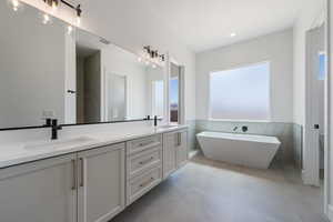 Full bathroom featuring healthy amount of natural light, double vanity, tile walls, a wainscoted wall, and a soaking tub