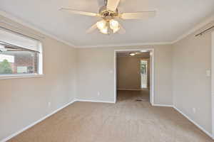 Carpeted spare room featuring baseboards, crown molding, and a ceiling fan
