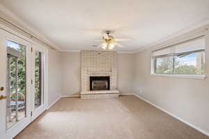 Unfurnished living room featuring a ceiling fan, carpet, baseboards, ornamental molding, and a brick fireplace