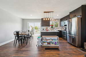 Kitchen featuring appliances with stainless steel finishes, light countertops, dark wood-type flooring, a textured ceiling, and a center island