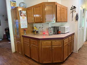 Kitchen featuring white microwave, dark wood-style floors, brown cabinets, and light countertops