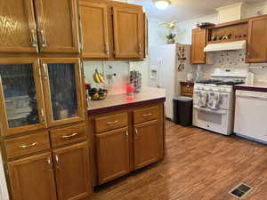Kitchen with white appliances, under cabinet range hood, brown cabinetry, open shelves, and wood finished floors