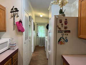 Kitchen with white appliances, a textured ceiling, brown cabinets, wood finished floors, and crown molding
