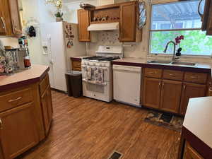 Kitchen with white appliances, a sink, under cabinet range hood, dark wood finished floors, and brown cabinets