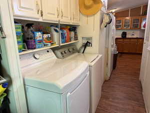 Clothes washing area with washing machine and dryer, dark wood-style flooring, and cabinet space