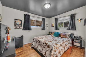 Bedroom with wood finished floors, lofted ceiling, and baseboards