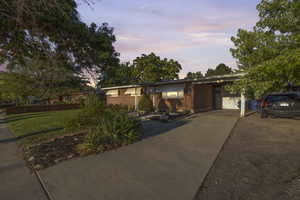 View of front of home featuring brick siding, driveway, a yard, and a carport at twilight!