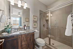 Bathroom with a stall shower, toilet, vanity, and ceiling fan