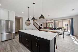 Kitchen featuring freestanding refrigerator, dark cabinets, white cabinets, light wood finished floors, and light countertops