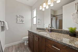 Bathroom featuring a shower with curtain, toilet, vanity, baseboards, and wood finished floors