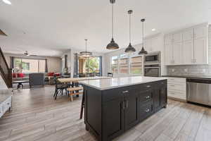 Kitchen featuring appliances with stainless steel finishes, white cabinets, open floor plan, dark cabinetry, and light wood-style floors