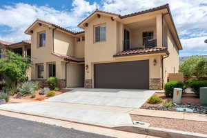 Mediterranean / spanish house with a balcony, a tiled roof, a garage, stone siding, and stucco siding