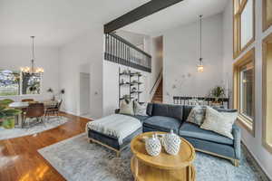 Living room featuring high vaulted ceiling, stairs, a chandelier, wood finished floors, and baseboards