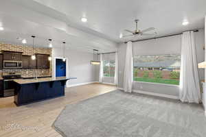 Kitchen with stainless steel appliances, a kitchen bar, ceiling fan, dark brown cabinets, and a kitchen island with sink