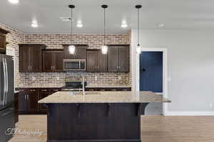 Kitchen featuring appliances with stainless steel finishes, a sink, a breakfast bar area, light wood-style floors, and dark brown cabinets