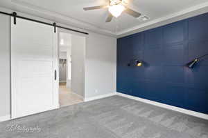 Tiled spare room featuring carpet flooring, a ceiling fan, a barn door, and a tray ceiling