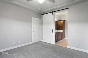 Unfurnished bedroom with a barn door, light colored carpet, baseboards, connected bathroom, and a sink