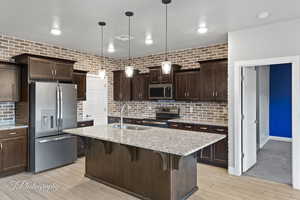Kitchen featuring appliances with stainless steel finishes, a sink, a breakfast bar, backsplash, and dark brown cabinets