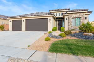 View of front facade featuring stucco siding, a garage, driveway, stone siding, and a tiled roof
