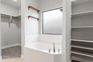 Bathroom featuring a walk in closet, a garden tub, and tile patterned floors