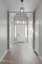 Foyer entrance with a raised ceiling, baseboards, light wood-type flooring, and a textured ceiling