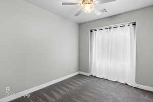 Empty room with dark carpet, baseboards, and ceiling fan
