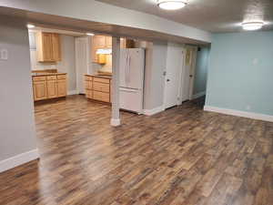 Basement kitchen with freestanding refrigerator, dark wood-style flooring, baseboards
